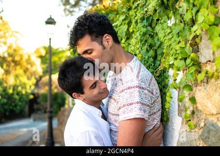 Un garçon embrassant son petit ami. Jeune couple gay amoureux. Deux jeunes garçons gay en plein air en été dans une rue de banlieue. Fier couple de blanc brun garçon Banque D'Images
