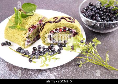 Un rouleau d'éponge en tranches avec des bleuets et du thé au matcha sur une assiette blanche. Banque D'Images