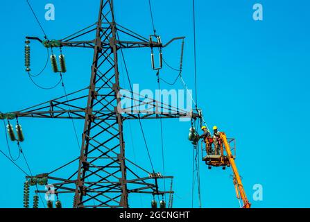 Dnepropetrovsk, Ukraine - 08.06.2021: Travailleurs de la tour de transmission de ligne haute tension avec grue et ciel bleu. L'Hydro linemen sur les relevages de rampe fonctionne Banque D'Images