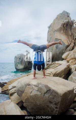 Homme hispanique sportif faisant une main sur un rocher contre une vue sur l'océan Banque D'Images