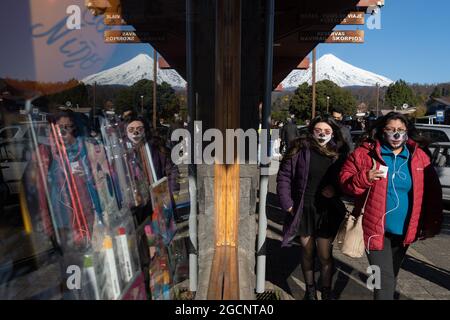 Pucon, Araucania, Chili. 9 août 2021. Les femmes avec masque facial traversent le centre de Pucon et se reflètent dans un verre d'un local commercial, et en arrière-plan le volcan Villarrica, dans le sud du Chili, au milieu de la pandémie de covid et de la faible contagion au niveau du pays. (Credit image: © Matias Basualdo/ZUMA Press Wire) Banque D'Images