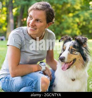 Bonne jeune femme passant du temps avec un joli chien de berger australien tacheté dans un pré vert le jour de l'été Banque D'Images