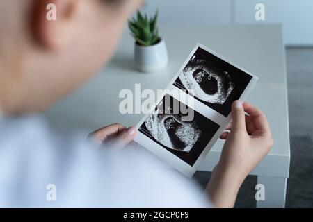 Vue arrière de la femme blanche enceinte inconnue tenant et regardant la photo de sa première échographie du concept de maternité de bébé Banque D'Images
