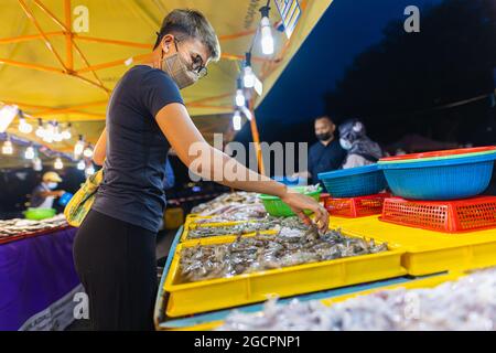 Marché nocturne de la cuisine de rue à Putrajaya, près de Kuala Lumpur. Une jeune fille asiatique achète des fruits de mer dans un marché nocturne. Femmes malaisiennes avec masque dans une rue Banque D'Images
