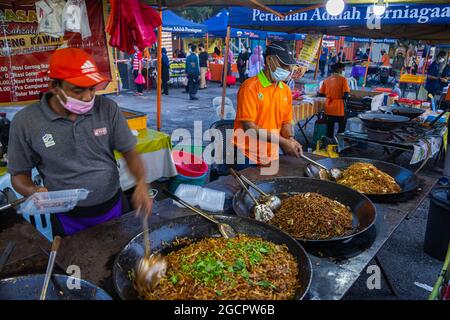 Les nouilles frites sont stockées dans un marché de nuit à Kuala Lumpur. Deux na vendant des nouilles traditionnelles d'un wok. En raison de la crise corona l'homme portant le visage ma Banque D'Images