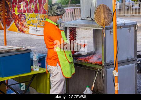 Magasin de poulet au miel sur le marché de nuit à Putrajaya, Kuala Lumpur. L'homme grille le poulet mariné sur un petit gril. La viande a une couleur rouge forte Banque D'Images