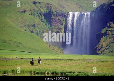 Femmes cavaliers devant la cascade, paysage vert et montagnes, Skogafoss, Islande Banque D'Images