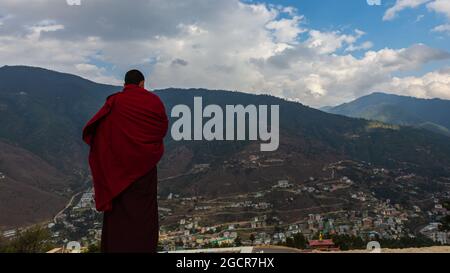 Un moine en robe rouge donne sur le paysage de montagne du royaume du Bhoutan près de la ville de Paro. Banque D'Images