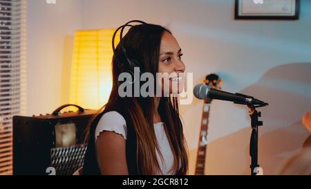 Gros plan sur une belle fille souriante dans un casque chantant sa chanson préférée sur la répétition en studio à la maison le soir. Banque D'Images