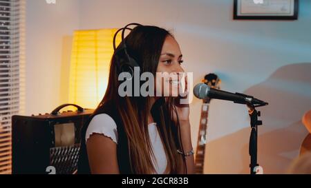 Chanteuse noire féminine en casque enregistrant sa nouvelle chanson en studio à domicile, chantant sensuellement dans le microphone Banque D'Images