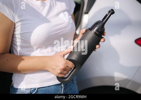 Femme tenir l'aspirateur portable devant la voiture. Belle jeune femme se prépare pour le nettoyage dans le garage. Gros plan des mains Banque D'Images