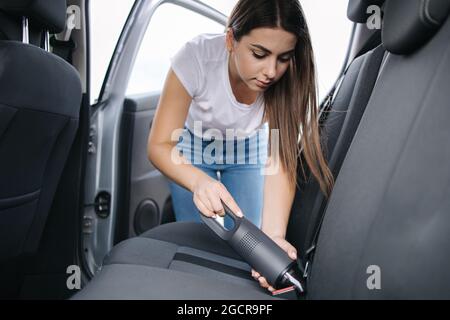 Femme passant l'aspirateur dans son siège arrière dans sa voiture dans le garage à la maison. Femme utilisant un aspirateur portable pour enlever la poussière et la saleté. Nettoyage de l'intérieur de la voiture Banque D'Images