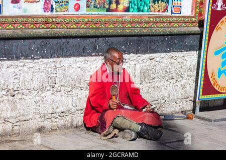 Lhassa, Tibet, Chine - 15 novembre 2019 : vieil homme tibétain avec béquilles et roue de prière tibétaine, assis sur le côté de la route près du temple de Jokhang. El Banque D'Images