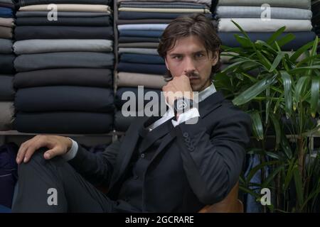 Beau homme en costume noir assis dans l'atelier et regardant l'appareil photo avec l'espace de copie. Yeux sérieux. Portrait en gros plan. Photo de haute qualité Banque D'Images