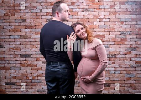 Un homme adulte se tient avec son dos à une femme enceinte souriante contre un mur de briques rouges Banque D'Images