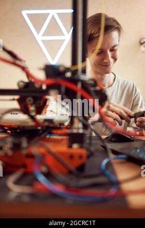 Commandes de réglage mâles anonymes à angle élevé sur l'imprimante 3D lors de la création d'un modèle en plastique dans un atelier Banque D'Images