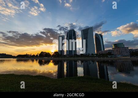 Gratte-ciel au coucher du soleil, en face d'un lac avec des reflets des bâtiments. Magnifique coucher de soleil coloré derrière les maisons hautes. Quartier des affaires ilumina Banque D'Images