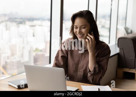 Bonne femme d'affaires parlant sur un smartphone au travail avec un ordinateur portable Banque D'Images