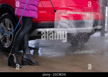 Gros plan d'une femme qui lave la voiture avec de l'eau sous haute pression au lavage de voiture en libre-service. Banque D'Images