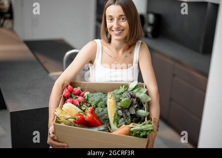 Femme avec des légumes frais emballés dans une boîte en carton à la cuisine Banque D'Images