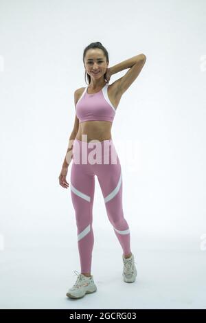 Jeune femme belle tenue marchant et tenant son cou. Isolée sur fond blanc. Chaussures de sport roses, blanches. Photo de studio. Haute qualité Banque D'Images