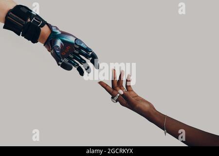 Prothèse de main mâle cyborg atteignant la main africaine noire humaine femelle. Concept de progression des mains en contact Banque D'Images