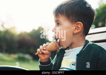 Beau portrait de bébé mangeant de glace dans le parc sur banc. L'été en plein air. Mets sucrés. Banque D'Images