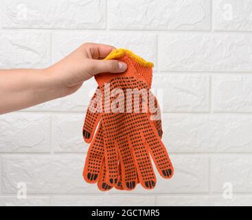 la main femelle tient des gants de travail en tissu orange sur un fond blanc. Vêtements de protection pour les travailleurs manuels, gros plan Banque D'Images