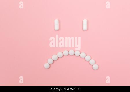 Préjudice pharmaceutique. Sad Smiley visage fait de pilules blanches, couché sur le Backgrond rose. Industrie pharmaceutique mondiale et médicaments Banque D'Images