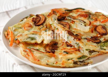 Yachaejeon, crêpe de légumes de patate douce, courgettes, oignons, champignons, piment vert sur une assiette blanche, cuisine coréenne Banque D'Images