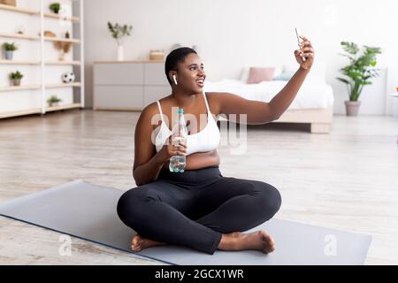 Femme noire de taille plus prenant le selfie en pause après l'entraînement à domicile, le chat vidéo à l'entraîneur personnel sur le Web à la maison Banque D'Images