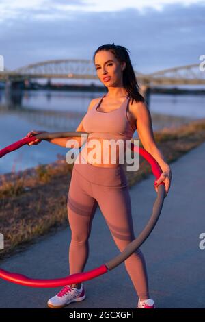 Jeune femme sportive tenant le hula hoop sur la rive pendant le coucher du soleil Banque D'Images