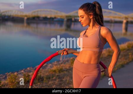 Bonne jeune femme sportive avec hula hoop posant à la rive de la rivière Banque D'Images