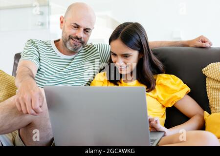 Un père heureux et une fille adolescente regardant quelque chose dans son ordinateur portable ou ayant un appel vidéo assis dans le canapé. Concentrez-vous sur elle Banque D'Images