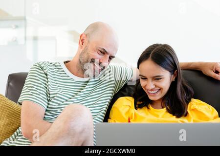 Père heureux et fille de l'adolescence regardant quelque chose de drôle dans son ordinateur portable ou ayant un appel vidéo assis dans le canapé Banque D'Images