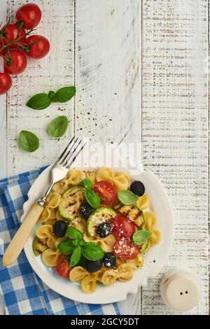 Pâtes salade fiocchi aux légumes courgettes grillées, tomates cerises, olives, basilic et parmesan dans une assiette blanche sur ardoise légère, pierre ou bétons Banque D'Images