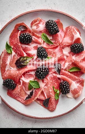 Fond de nourriture tranches de jambon de prosciutto coppa di parme avec basilic et mûre sur plaque légère. Orientation verticale Banque D'Images