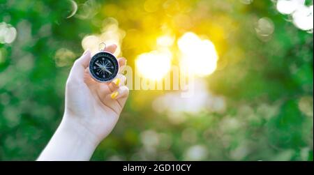 Main avec boussole sur fond vert flou avec un reflet du soleil au coucher du soleil Banque D'Images