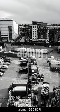 Prise de vue verticale en niveaux de gris de voitures dans un parking et de grands bâtiments en arrière-plan Banque D'Images