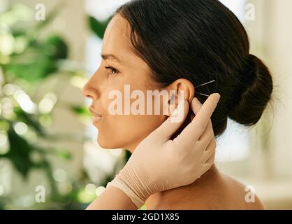 Femme ayant acupression d'oreille ou acuponcture d'oreille pour son traitement de maladies, vue latérale. Acupuncture, réflexologie, médecine traditionnelle chinoise Banque D'Images