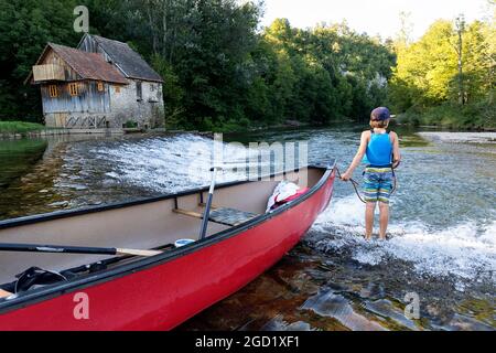 Un garçon portant un gilet de sauvetage guidant un canoë le long d'un brise-lames reliant la Slovénie et la Croatie, passant devant un ancien moulin à travers la rivière Kolpa Banque D'Images