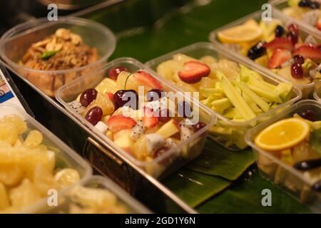 Marché de nuit en Thaïlande: En boîte, prêt à manger des ensembles de fruits tropicaux et de baies sur un stand lumineux Banque D'Images