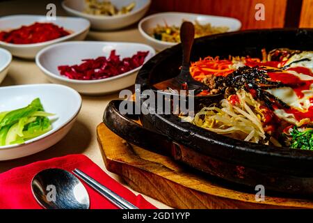 Bibimbap de bœuf chaud coréen servi dans une marmite en pierre de dolsot avec des plats d'accompagnement en banchan Banque D'Images