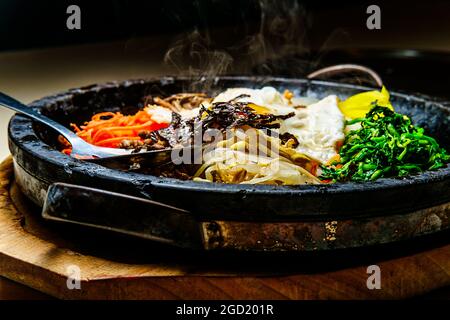 Bibimbap de bœuf chaud coréen servi dans une marmite en pierre de dolsot avec des plats d'accompagnement en banchan Banque D'Images