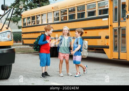 Enfants garçons et filles enfants élèves debout et parlant près de l'autobus scolaire jaune. Amis camarades de classe réunions après les vacances d'été. Éducation Banque D'Images