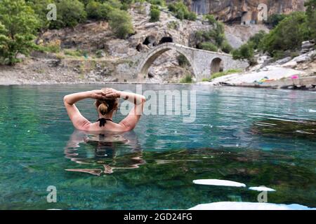Femme appréciant dans les bains thermaux à Benje, pouf pont en pierre derrière, rivière Lengarica, Përmet, Parc National Hotova-Dangell, Albanie Banque D'Images