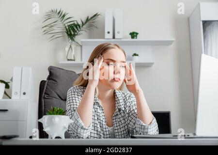 Une jeune femme contrariée en situation de stress fait du travail de bureau via un ordinateur portable. Dépression la jeune femme fatiguée a mal de tête en raison de problèmes d'affaires ou de la date limite au bureau à domicile. Banque D'Images