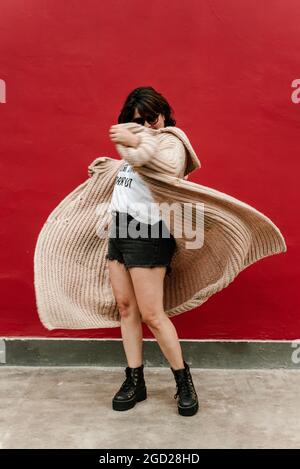 Image d'une femme qui joue avec son chandail le faisant voler. Foyer sélectif de femme tournant avec son pull à la main sur un fond rouge Banque D'Images