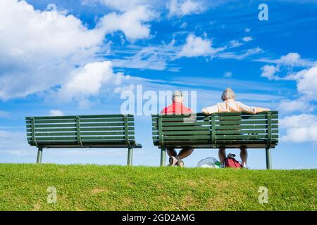 Vue arrière d'un couple âgé assis sur un siège donnant sur la mer par une journée ensoleillée. Banque D'Images