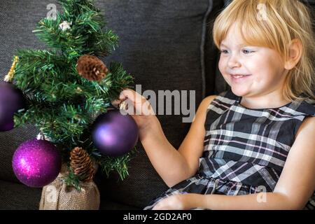 Sourire heureux belle fille décorant l'arbre de Noël avec des boules, assis sur le canapé Banque D'Images